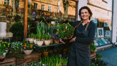 En smilende dame utenfor blomsterbutikken sin