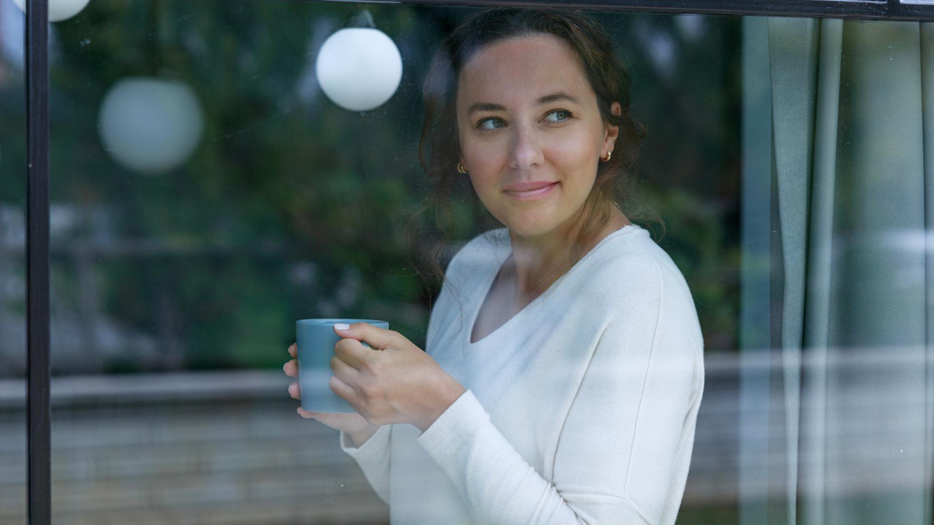 Dame holder kaffekopp og ser ut vindu