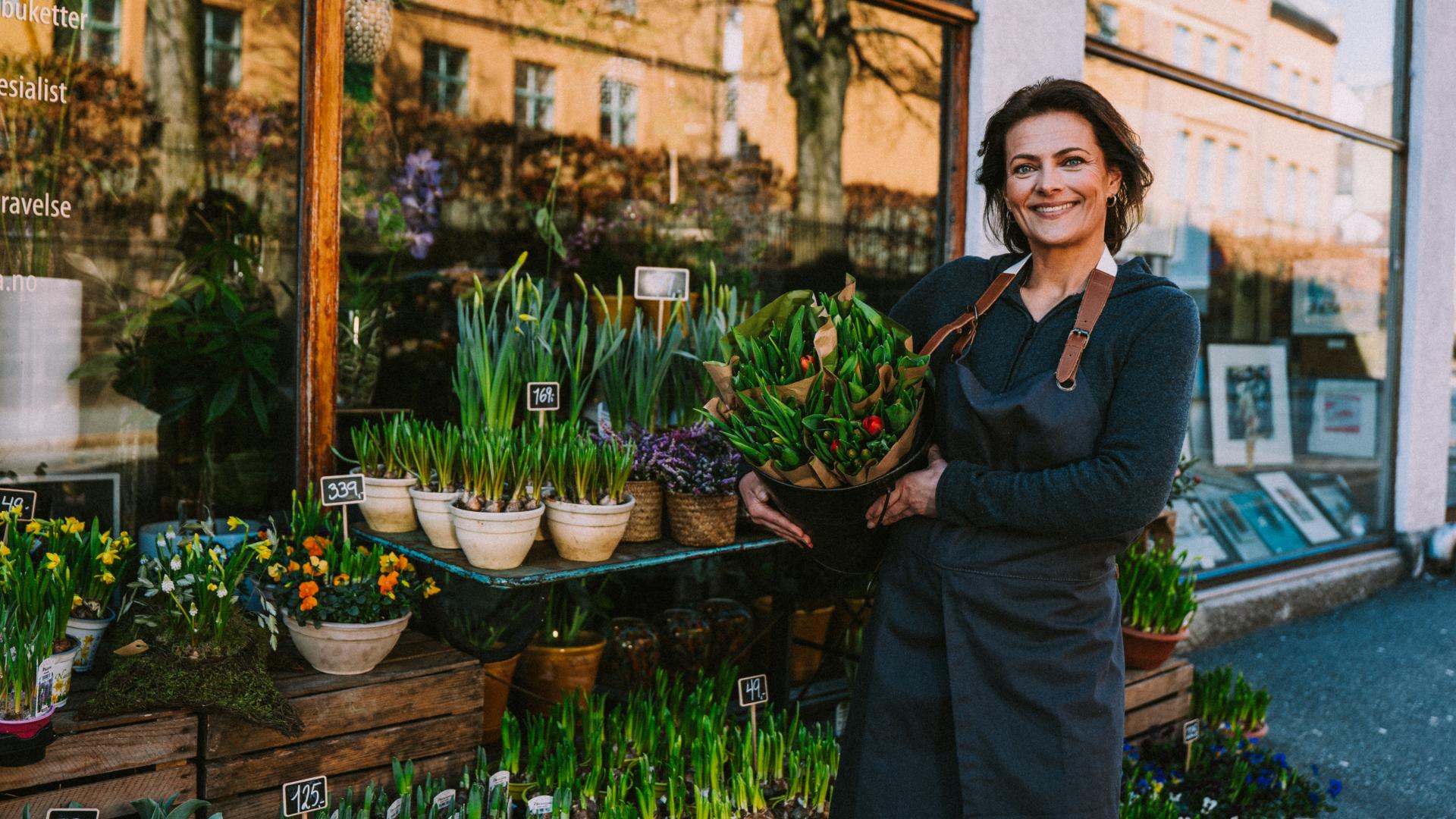 En smilende dame utenfor blomsterbutikken sin