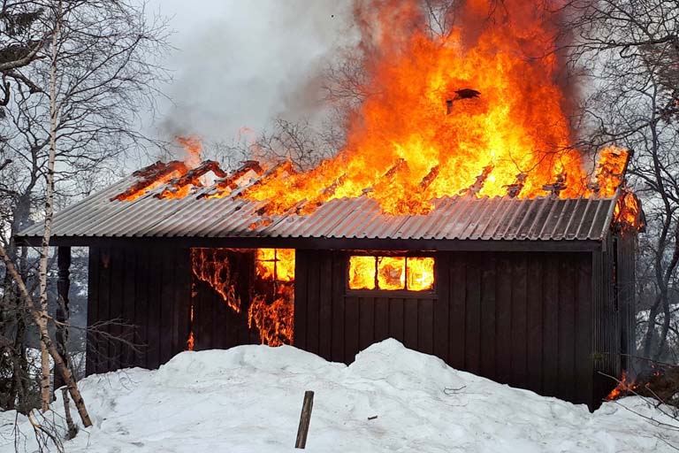 En hytte på fjellet står i full brann, en vinterdag.