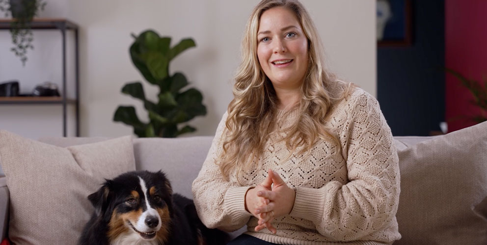 Hundretreneren Maren sitter på en sofa sammen med en sort hund