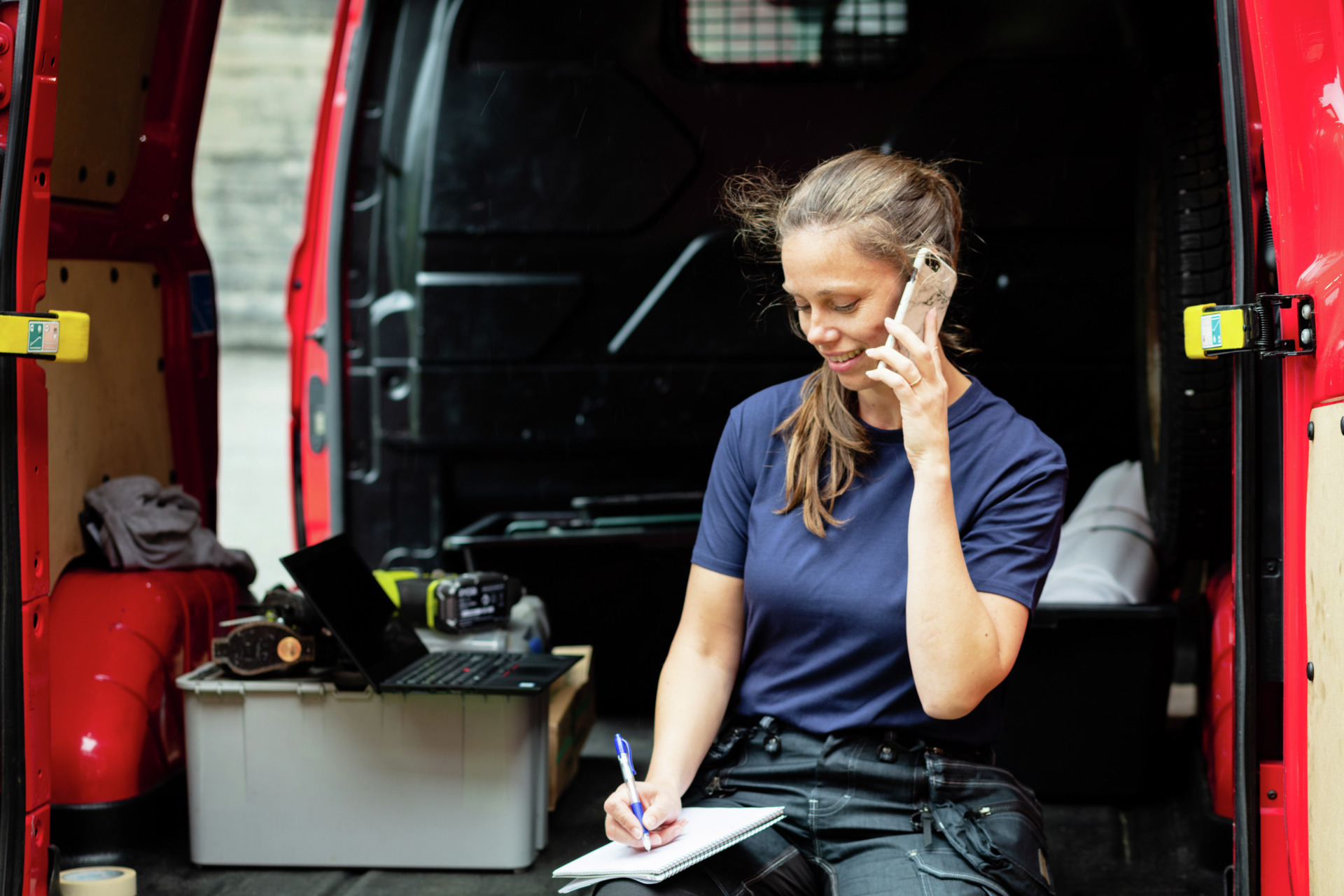 Kvinnelig håndverker sitter i varebil og snakker i telefon