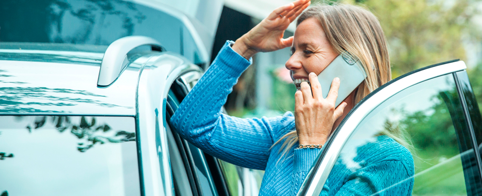 Kvinne står ved bilen sin og snakker i telefonen