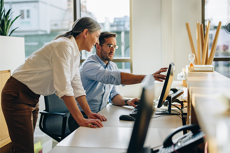 Mannlig og kvinnelig kollega sitter foran pc på kontor
