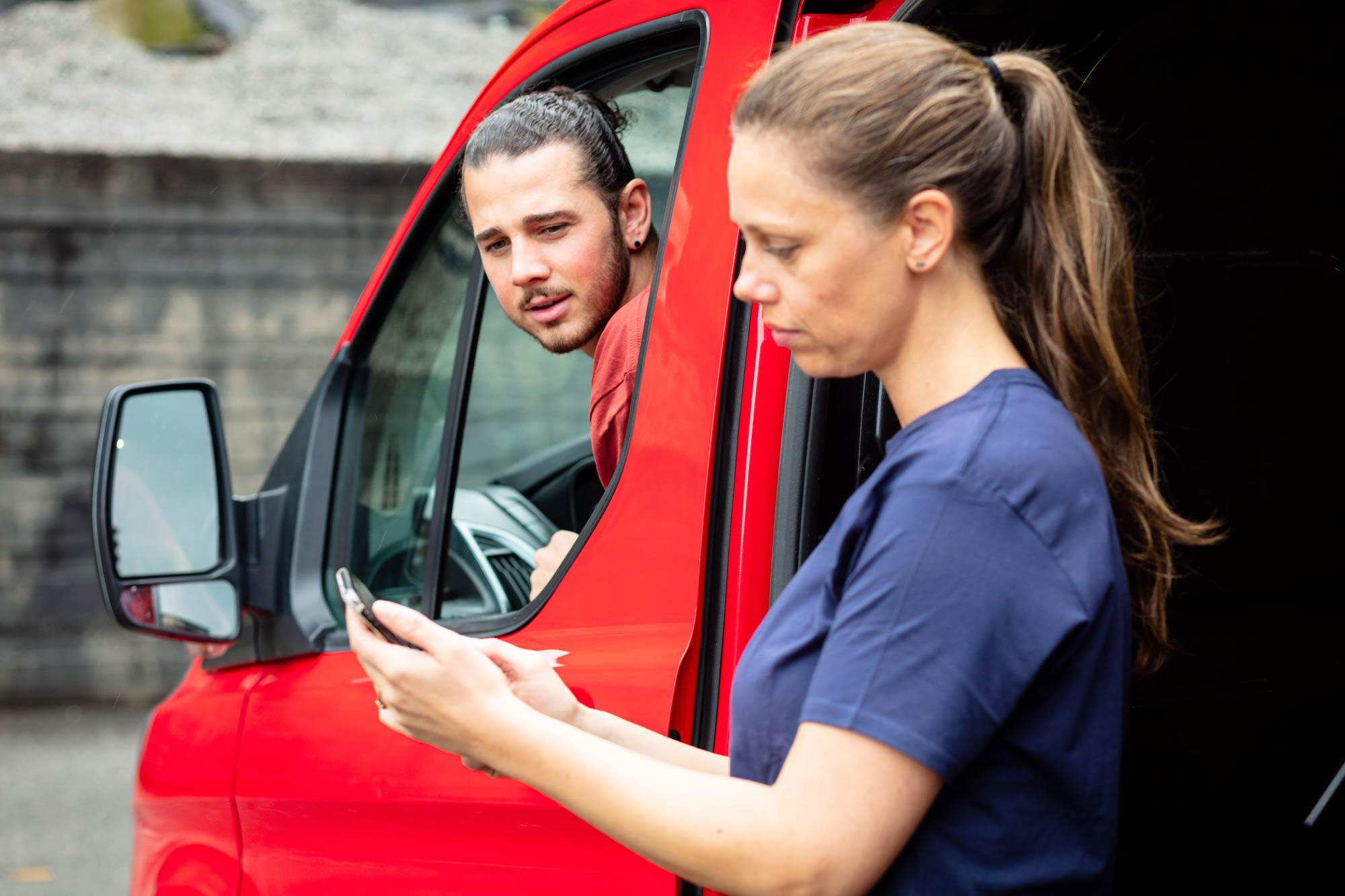 To håndverk-kollegaer ser på en telefon sammen utenfor firmabilen