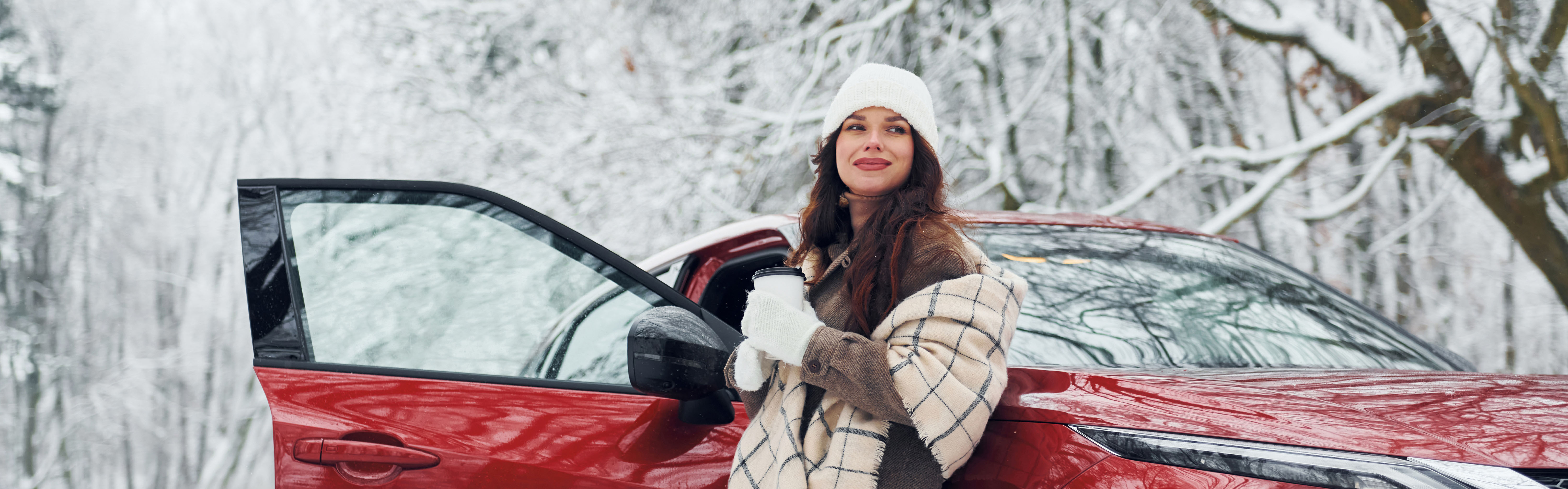 Dame drikker kaffe foran rød bil