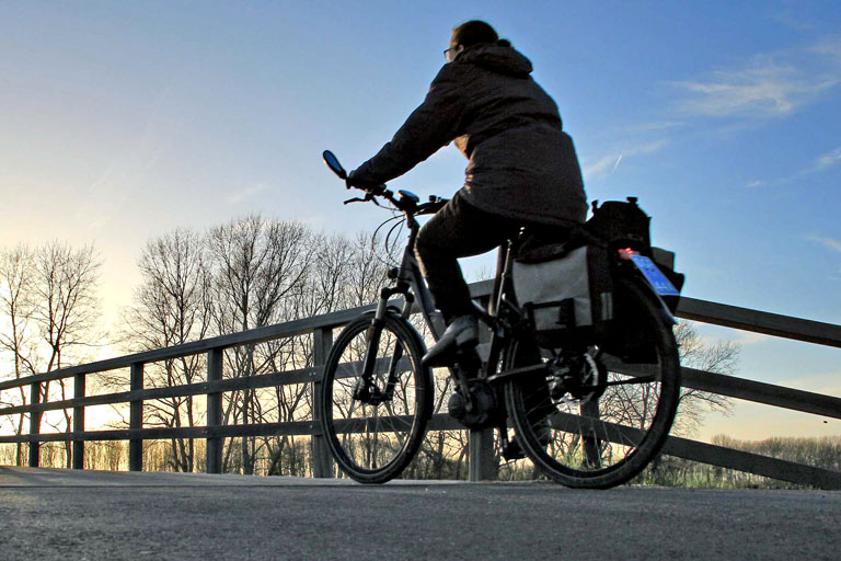 En dame sykler over en gangbro i soloppgangen, på en kald dag.
