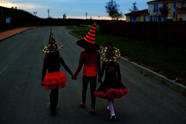 To jenter og en gutt som er utkledd som hekser på halloween, går på en vei