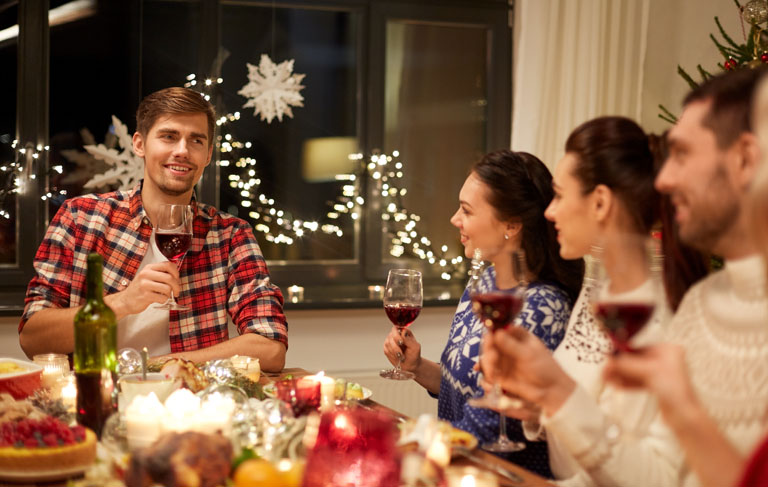 Folk som skåler med rødvinsglass, rundt et julebord
