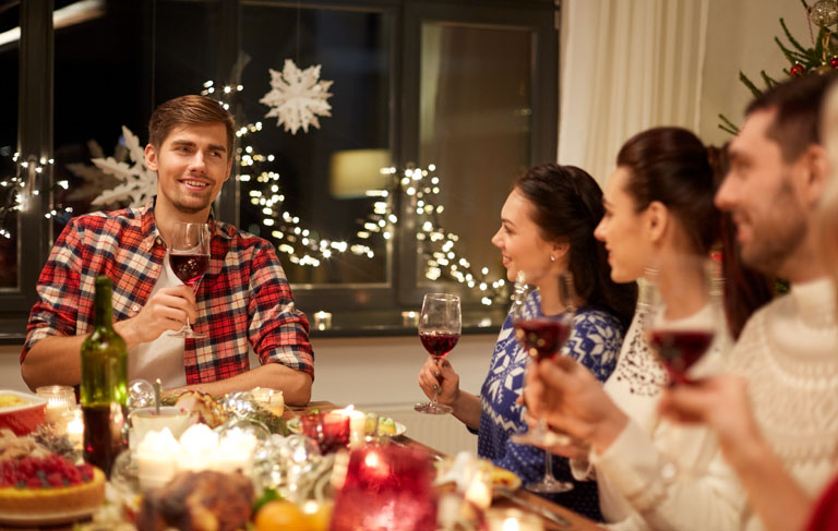 Folk som skåler med rødvinsglass, rundt et julebord