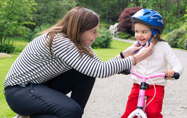 Mor fester hjelm på datteren, som sitter på en liten sykkel