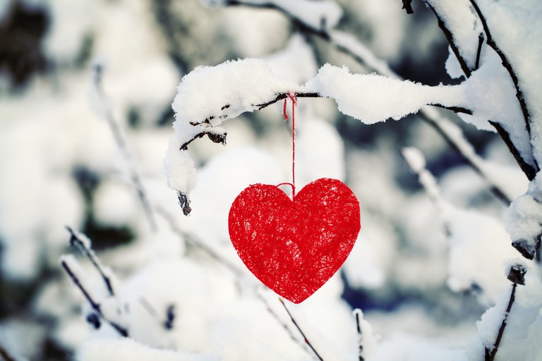 Et rødt julepynt-hjerte henger på en snødekt gren i skogen