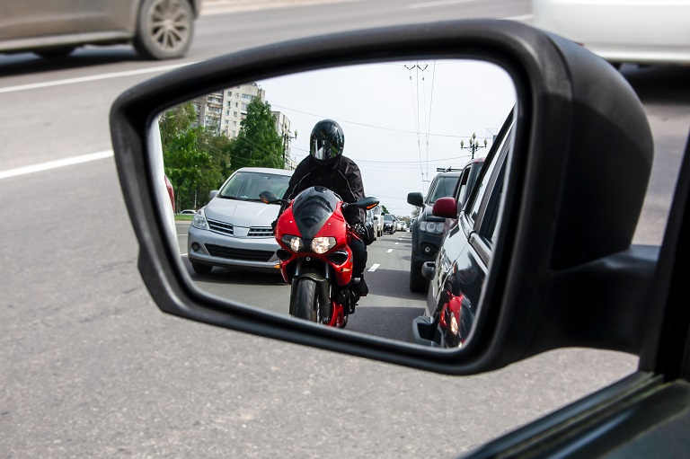 Nærbilde av sidespeil på bil, med en motorsyklist som nærmer seg bakfra