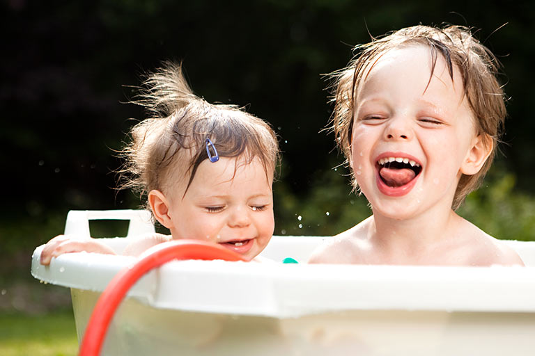 En liten gutt og lillesøsteren bader og koser seg, ute i en stamp, på en fin sommerdag.