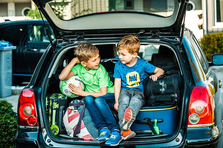 To små gutter sitter i fullpakket bagasjerom, klare for sommerferie
