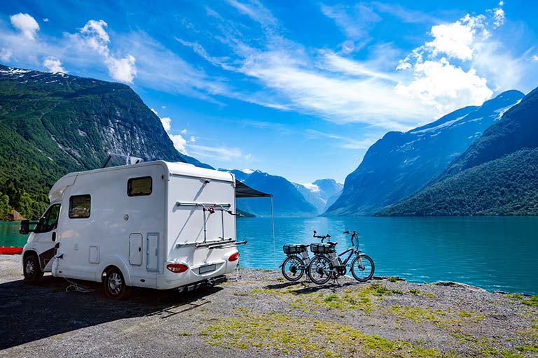 Bobil og sykler ved en norsk fjord, under blå himmel