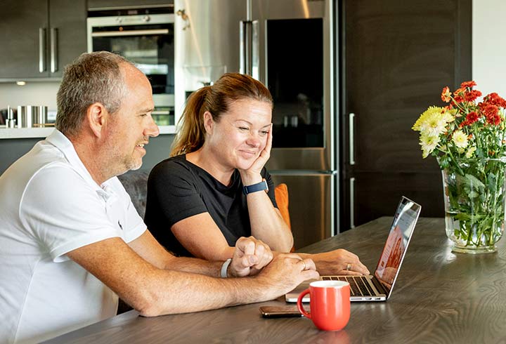 Par som sitter på kjøkkenet med laptop og kaffe