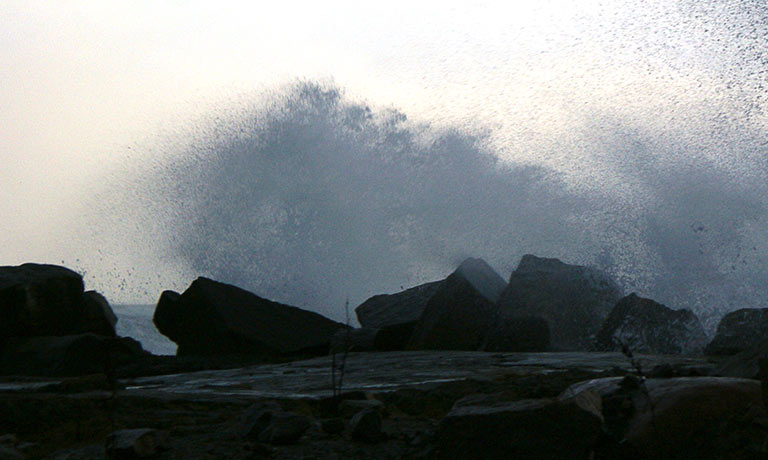 En stor bølge slår over kanten på en steinbrygge.
