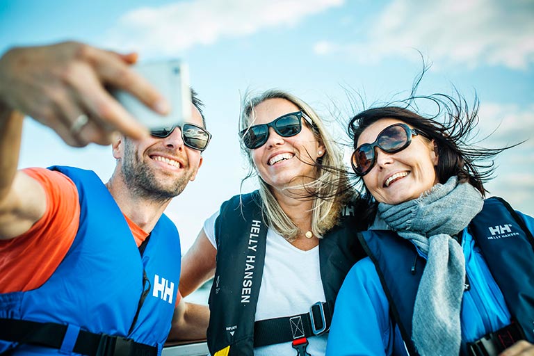 To damer og en mann i redningsvest og solbriller, tar selfie