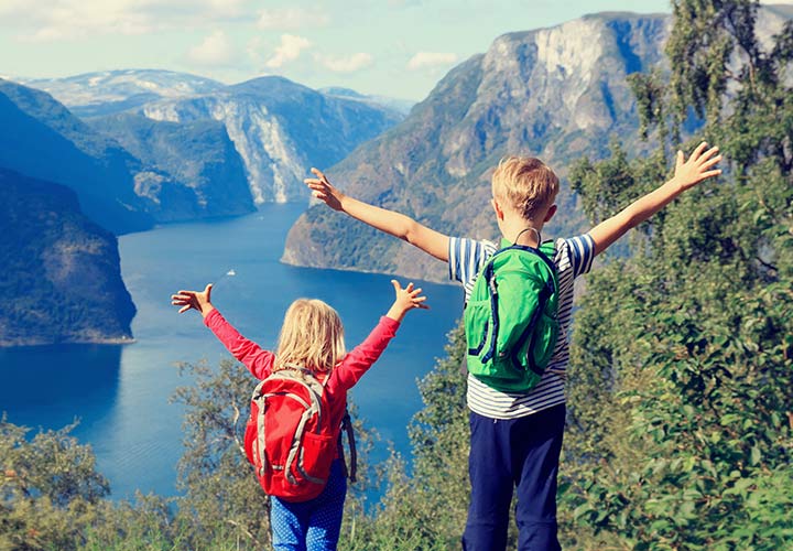 To barn med ryggsekk ser ut over en fjord fra fjellet