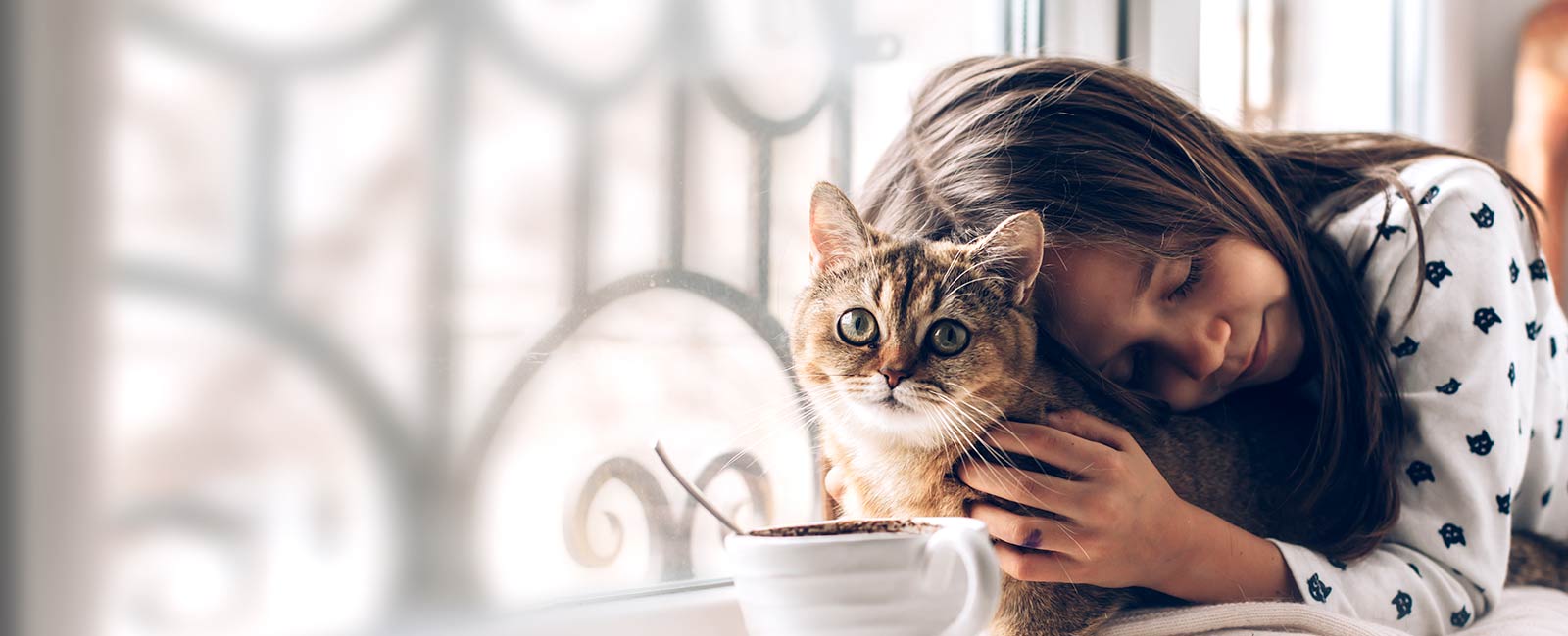 Ung jente som holder en katt tett inntil seg mens hun lukker øynene