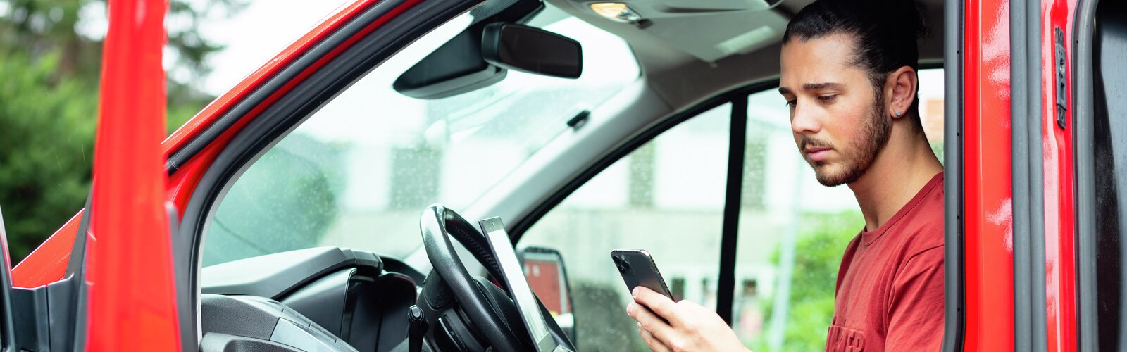 Mann sitter i varebil og ser på mobiltelefon